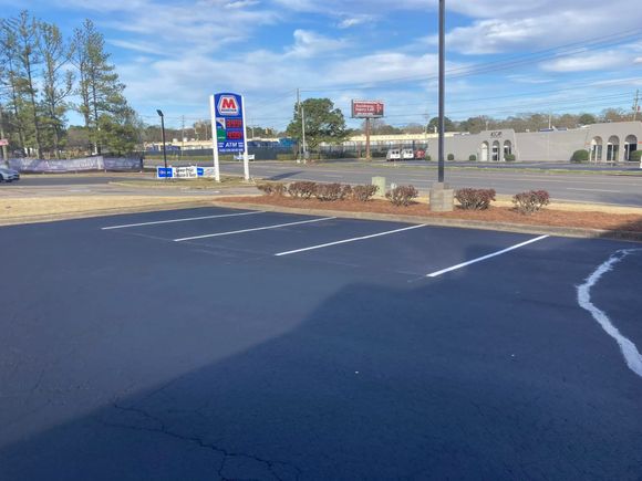 An empty parking lot with freshly painted white lines on asphalt, featuring a gas station sign in the background. An empty parking lot with freshly painted white lines on asphalt, featuring a gas station sign in the background.