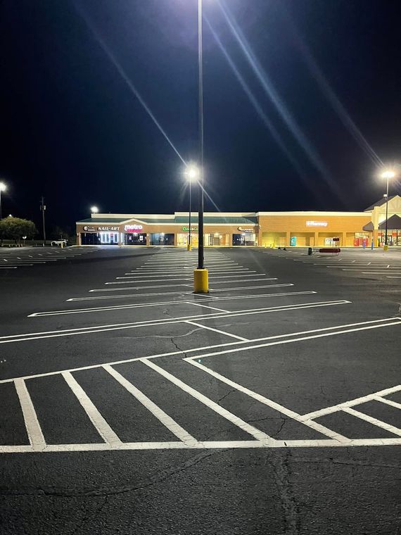 Empty parking lot at night with bright overhead lights illuminating the white lane markings and distant storefronts. Empty parking lot at night with bright overhead lights illuminating the white lane markings and distant storefronts.