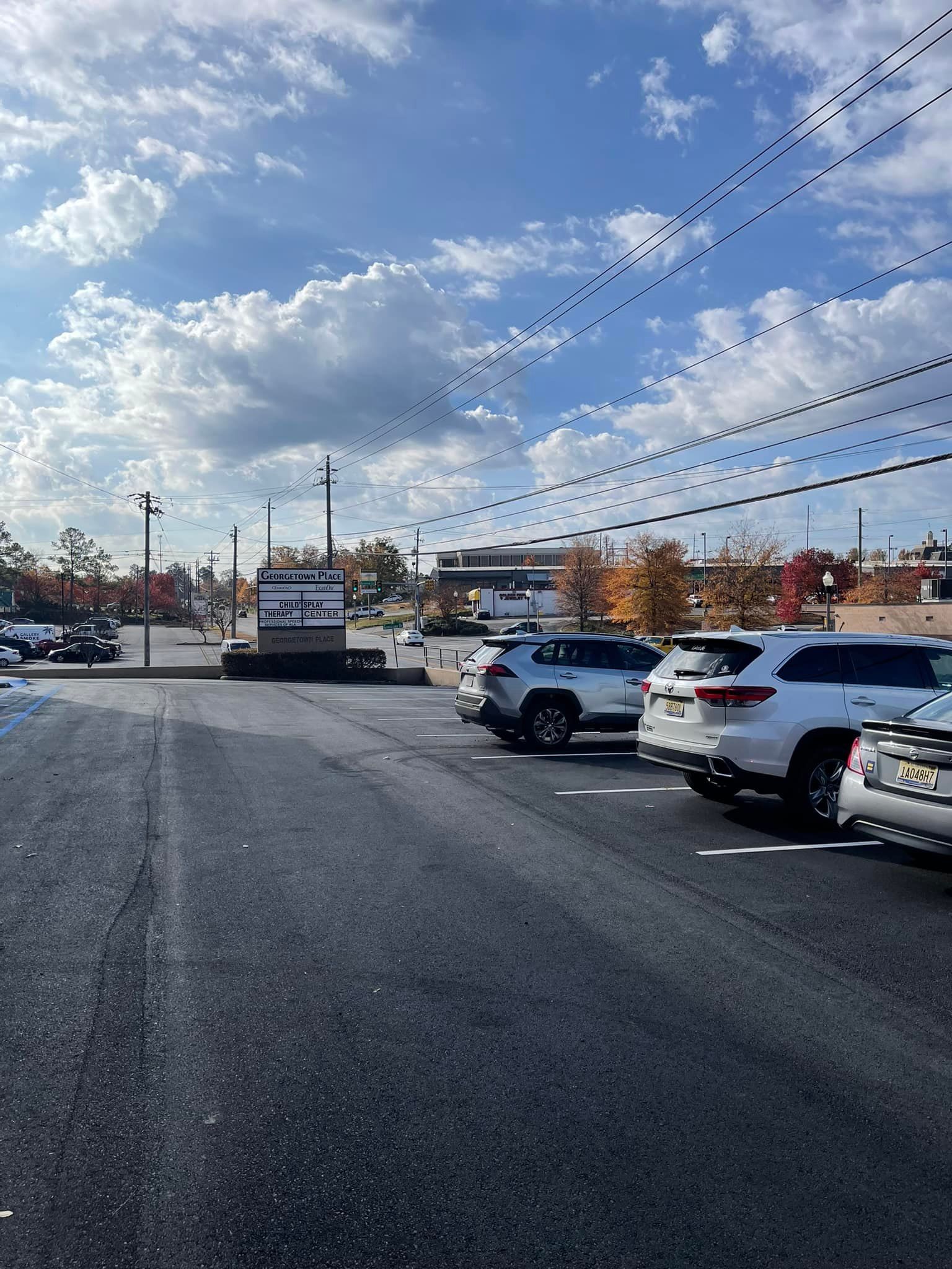 Parking lot with several parked cars under a partly cloudy sky, with a visible sign in the distance.
