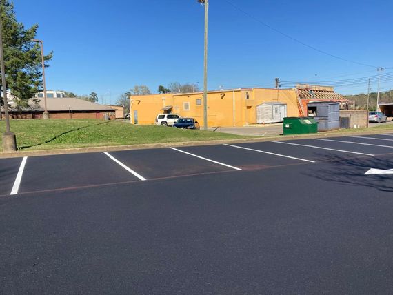 A newly paved parking lot with white painted lines in front of a yellow commercial building and grassy area. A newly paved parking lot with white painted lines in front of a yellow commercial building and grassy area.