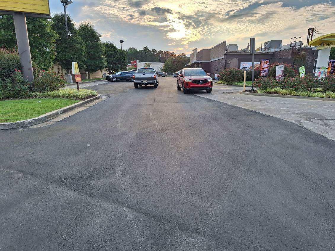 A gray pickup truck and a red SUV driving on an asphalt road near buildings at dusk.