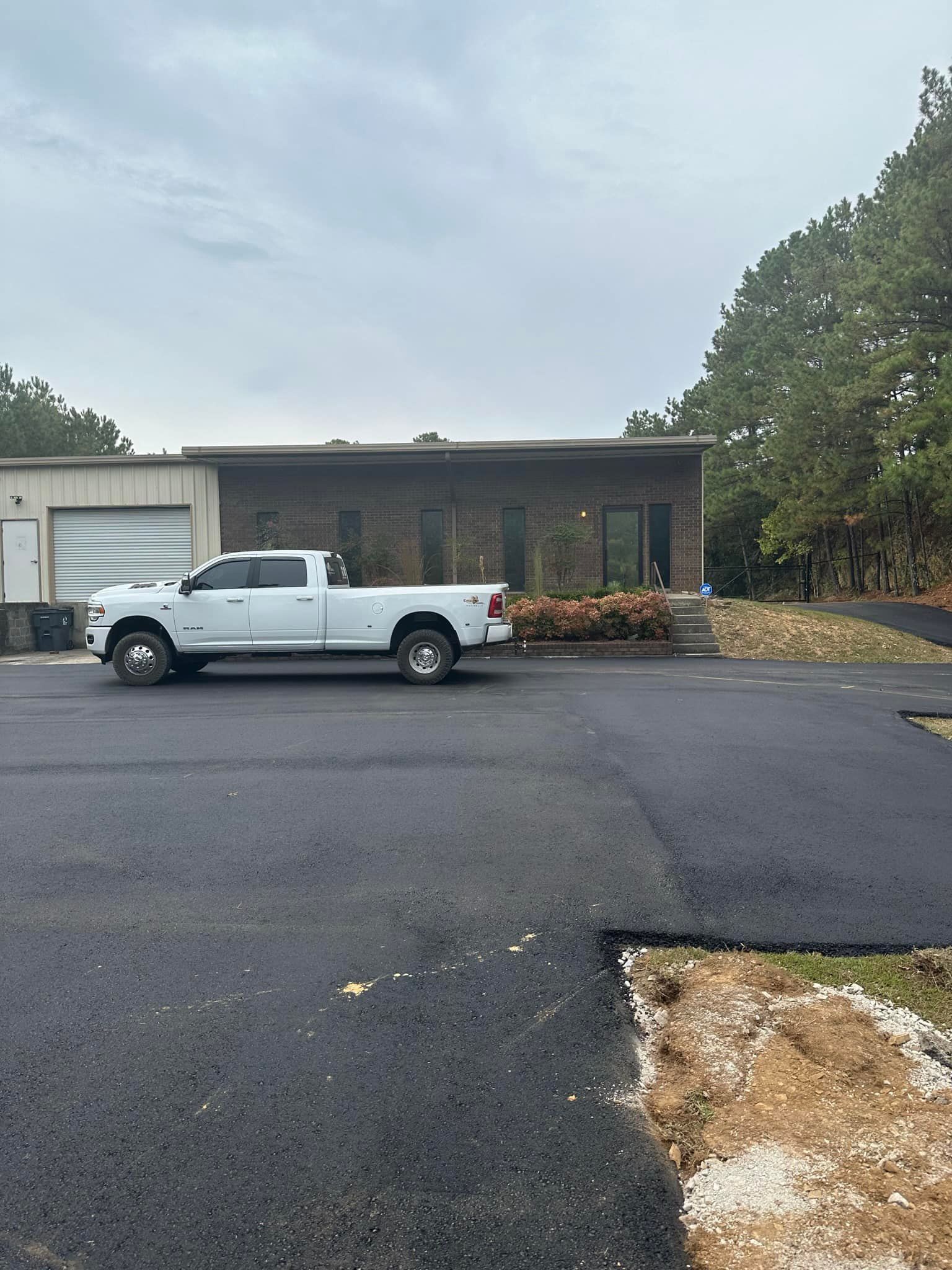 A white pickup truck parked in front of a brick building with a garage on a newly paved asphalt driveway.