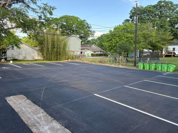 A newly paved parking lot with white painted lines and several green bins lined up along the far edge. A newly paved parking lot with white painted lines and several green bins lined up along the far edge.