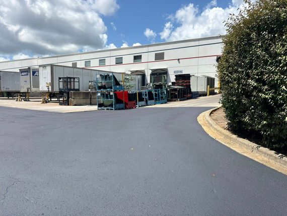 Loading dock of a white industrial building with several parked semi-trailers and racks of materials on the asphalt. Loading dock of a white industrial building with several parked semi-trailers and racks of materials on the asphalt.