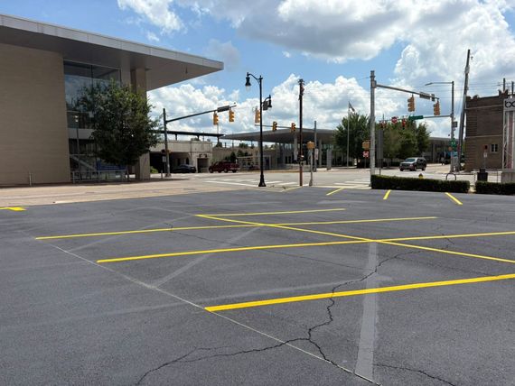 An empty parking lot with yellow-painted lines in front of a modern building and an intersection with traffic lights. An empty parking lot with yellow-painted lines in front of a modern building and an intersection with traffic lights.