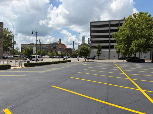 A freshly paved parking lot with white painted lines and a grass verge under a clear blue sky. A freshly paved parking lot with white painted lines and a grass verge under a clear blue sky.