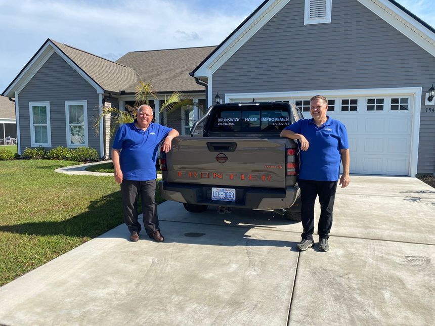 Two people in blue shirts standing beside a pickup truck in a driveway in front of a house