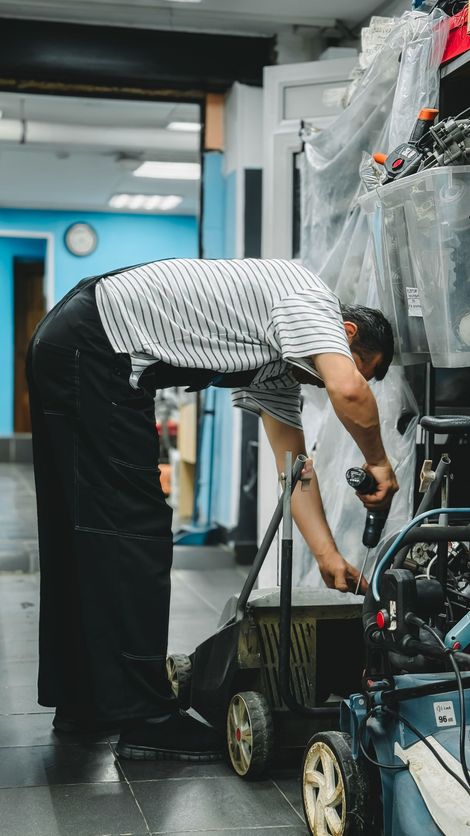 Mechanic bending over a scooter in a workshop, working on the engine with tools.