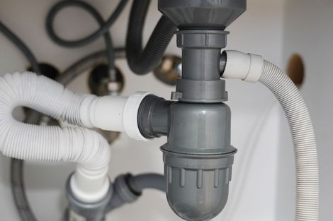 Under-sink plumbing with gray drain trap and white flexible hoses