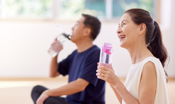 Man and woman sitting, drinking water bottles in a light-filled room.