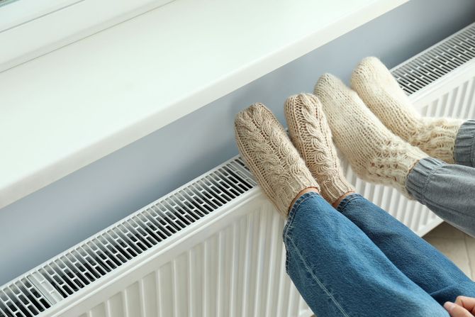 Deux personnes portant des chaussettes tricotées se réchauffent les pieds sur un radiateur.