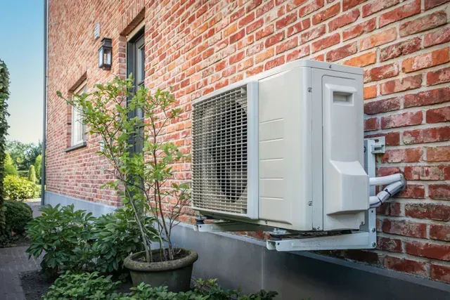 Un climatiseur blanc est monté sur le côté d'un bâtiment en briques.