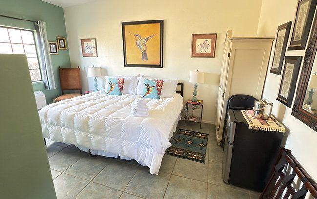 Bright bedroom with a white bed, framed art, tiled floor, and a window on the left.