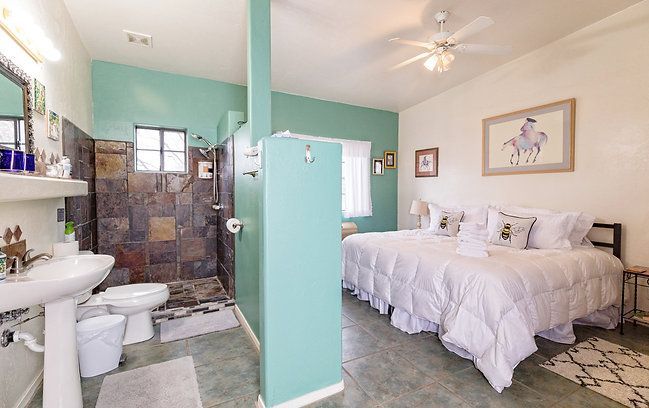 Bright bedroom with mint walls, white bed, and attached bathroom with tiled shower.