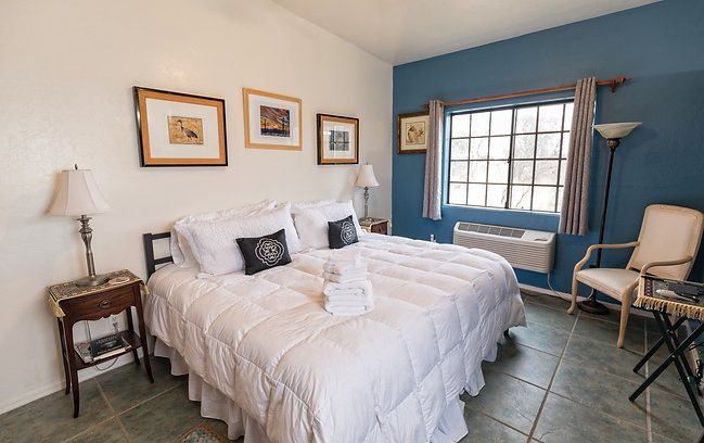 Bright bedroom with a white bed, blue accent wall, large window, and two chairs