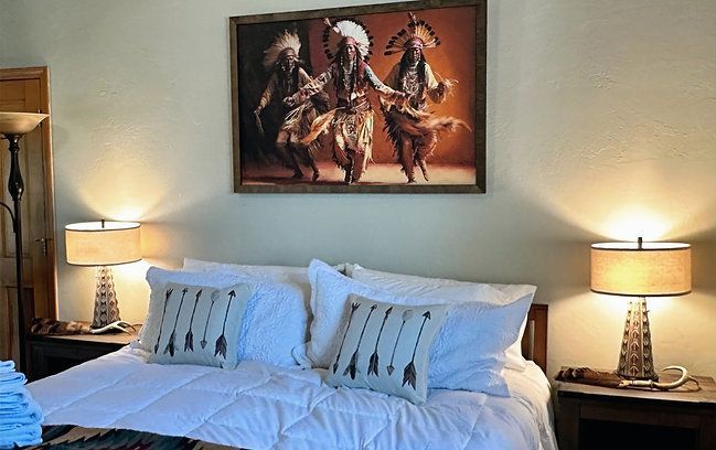 Bedroom with a neatly made bed, bedside lamps, and a framed horse painting above the headboard