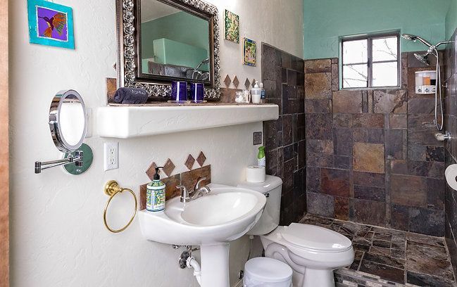 Bathroom with white pedestal sink, mirror, toilet, and tiled shower in teal and brown tones