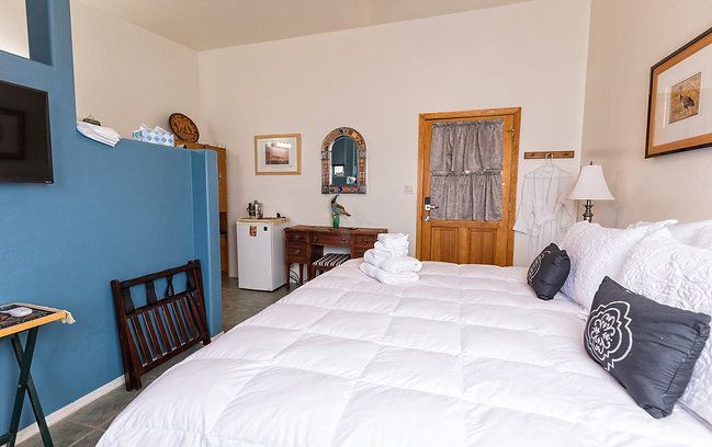 Cozy bedroom with a large white bed, blue accent wall, wooden door, and small desk by the window.