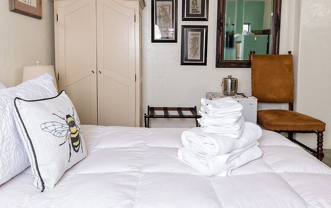 White bedroom with a made bed, folded towels, chair, wardrobe, and framed wall art