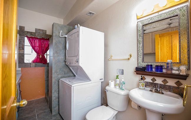 Small bathroom with stacked washer-dryer, toilet, sink, and ornate mirror next to a shower area.