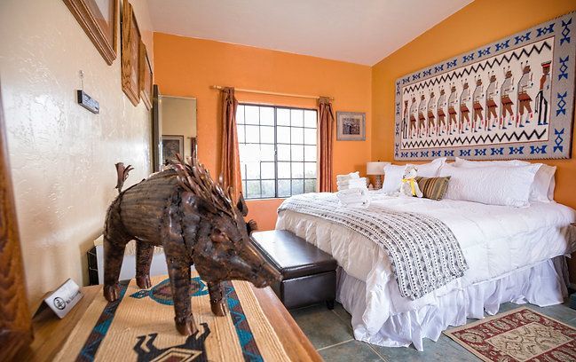 Elephant statue beside a bed in a bright orange bedroom with patterned wall art and a window.