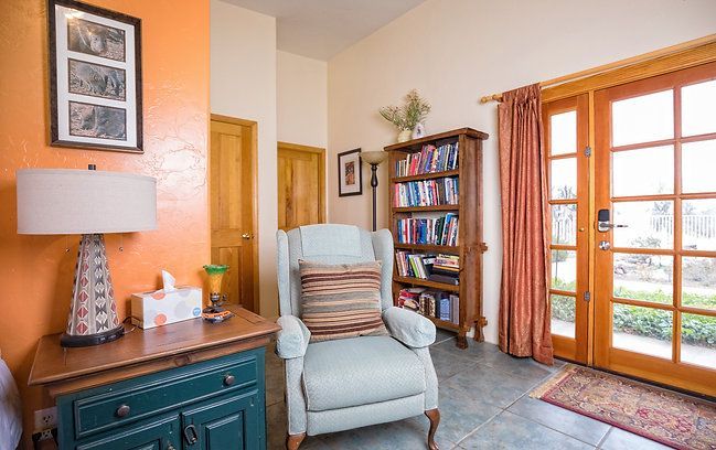 Cozy living room with blue armchair, teal cabinet, bookshelf, and French doors to a balcony