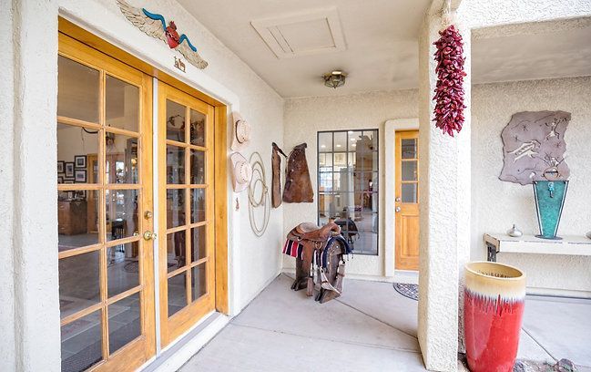 Covered porch with wooden double doors, hanging decorations, a chair, and a red drum table