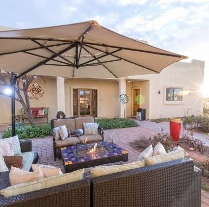 Patio seating area with wicker chairs, fire pit table, and large umbrella outside a modern house