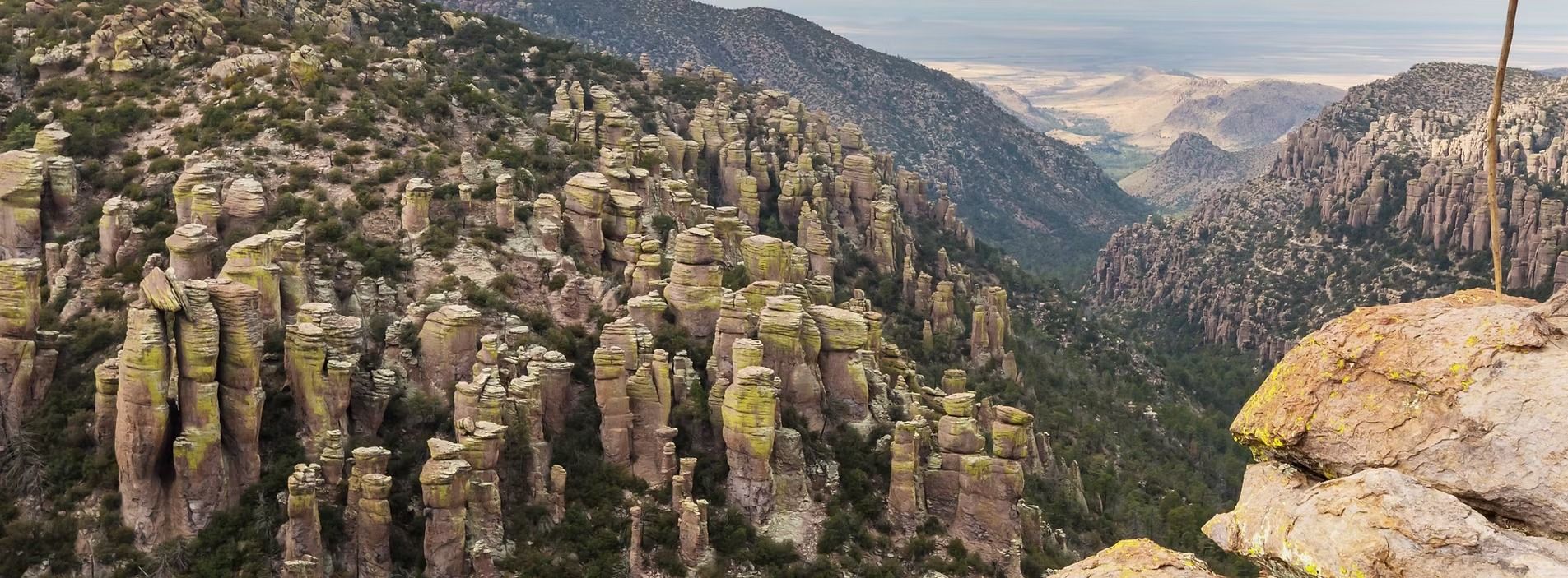 Rocky canyon with steep cliffs, narrow valley, and distant desert landscape under hazy light
