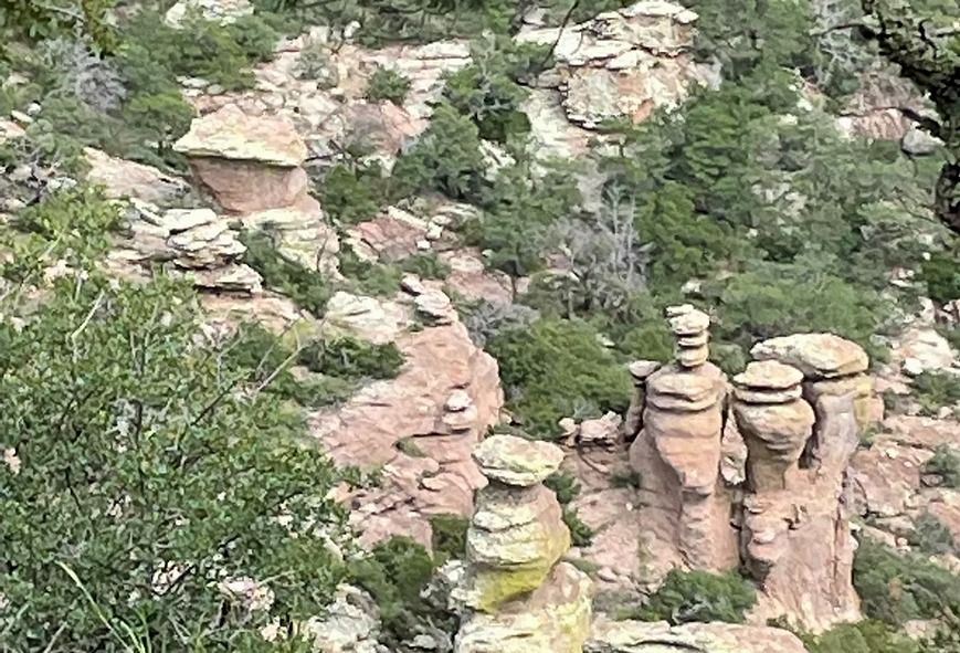 Rocky canyon with layered sandstone hoodoos and green shrubs on a steep cliffside.