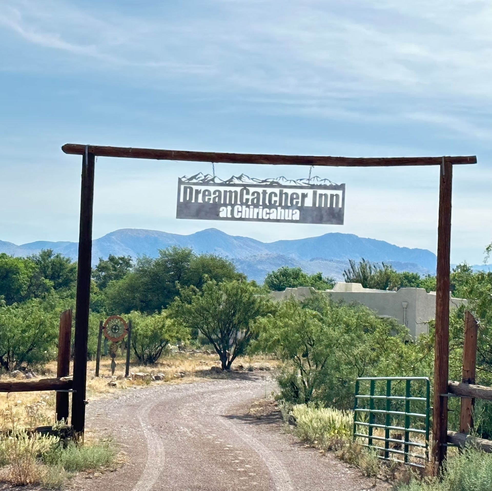 Entrance gate with DreamCatcher Inn sign, dirt path, trees, and distant mountains under a blue sky