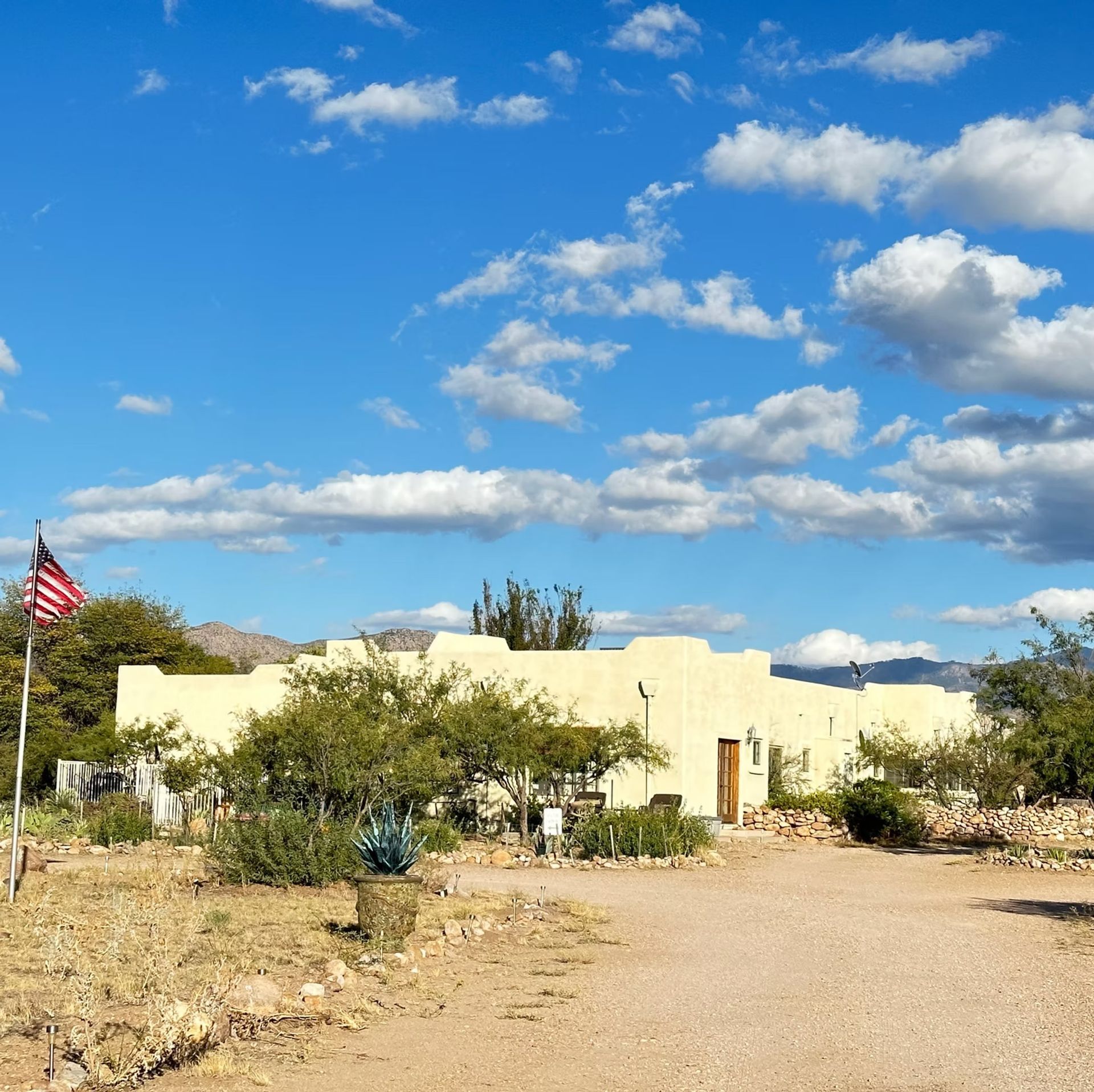 Desert home with an American flag under a bright blue sky with scattered clouds