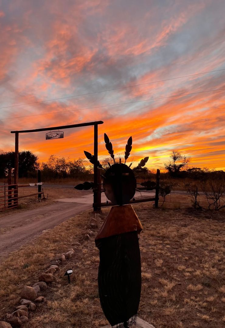 Sunset over a dirt road with a silhouetted native figure sculpture in the foreground