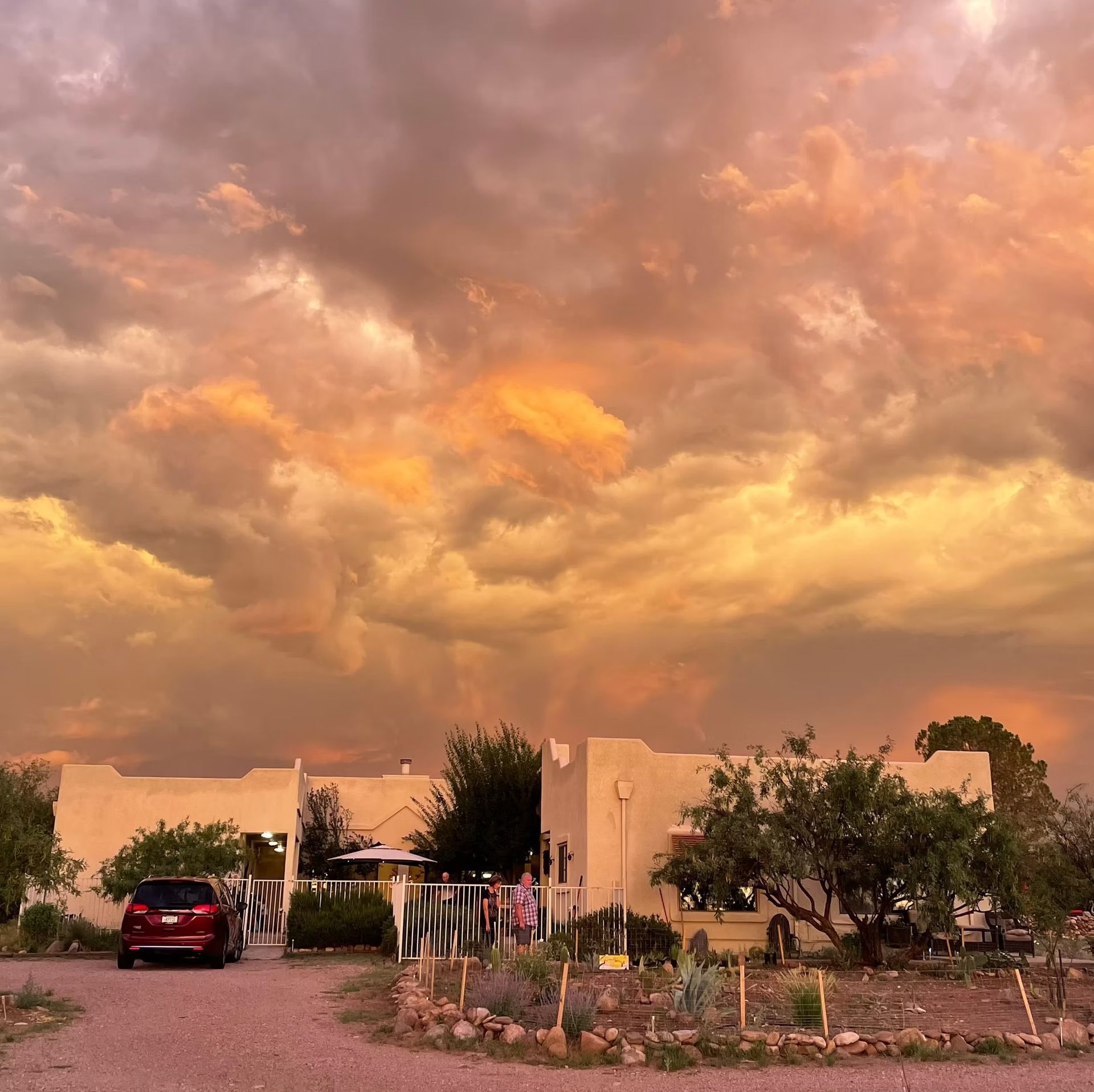 Desert home at sunset under dramatic orange clouds, with a car in the driveway and a garden in front
