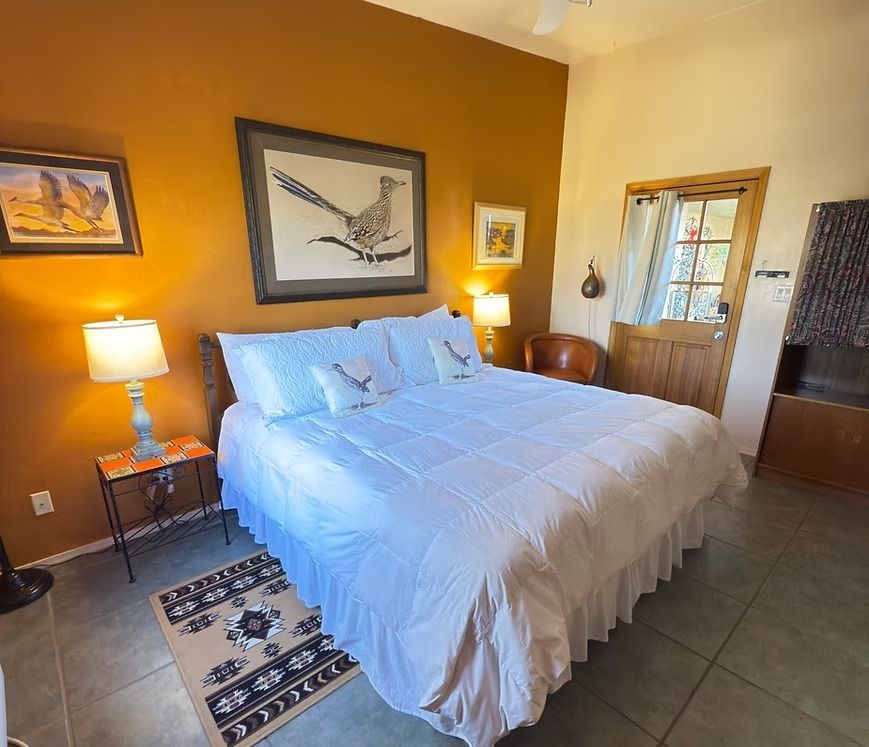 Cozy bedroom with white bed, mustard walls, framed art, bedside lamp, and tiled floor
