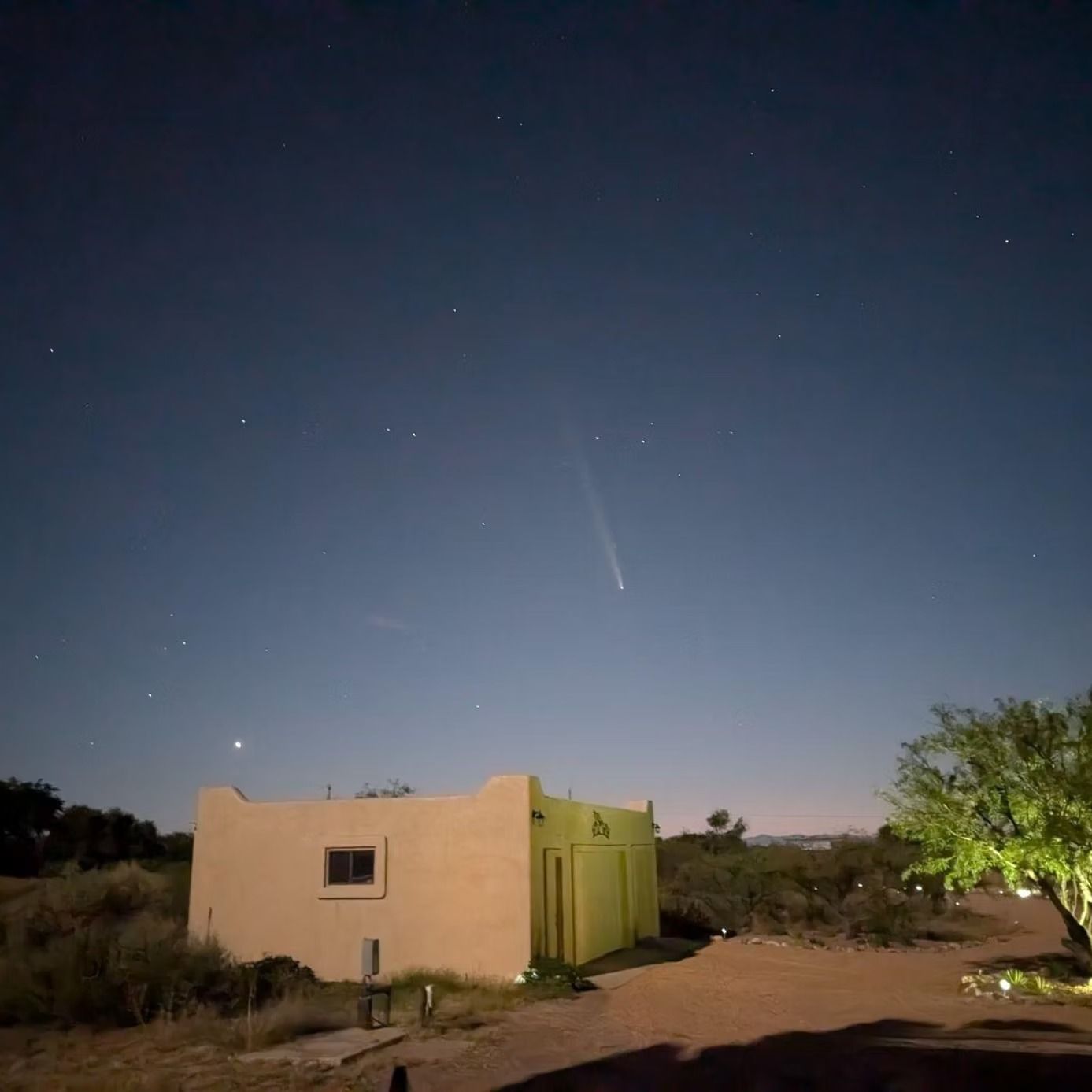 Small house at dusk under a starry sky, with a bright comet or meteor streaking above.