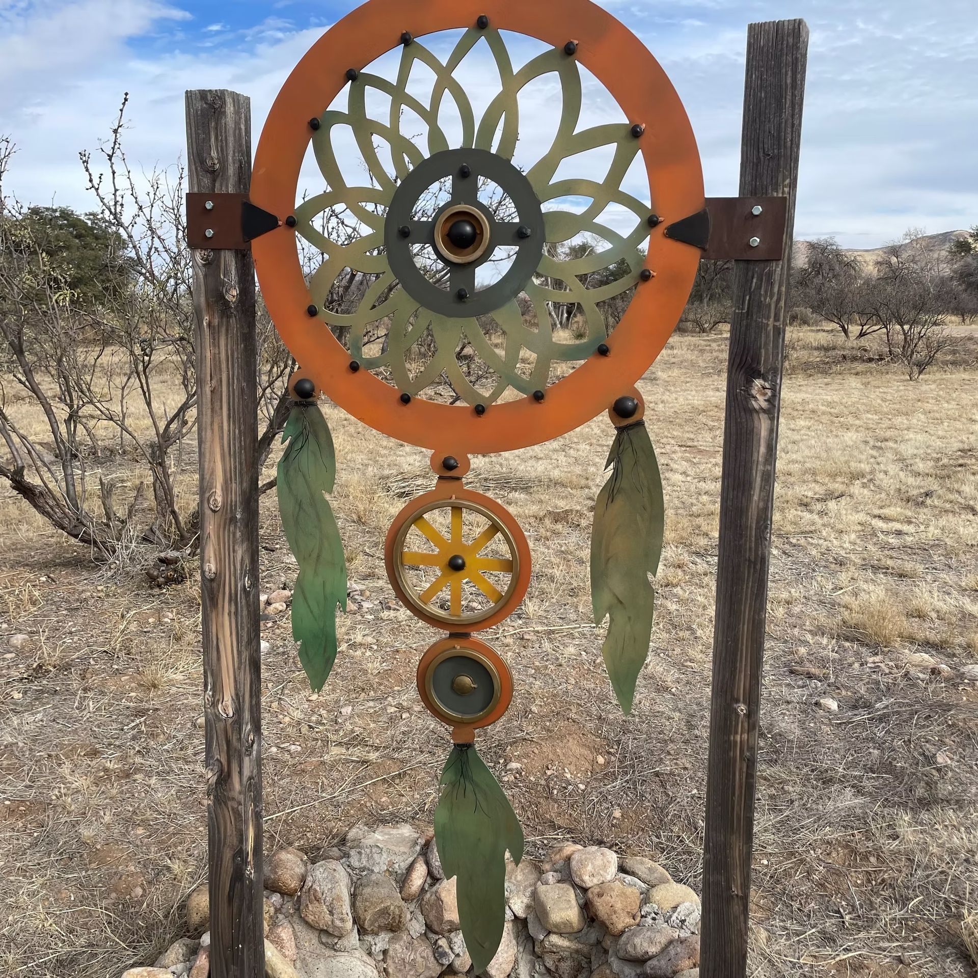 Colorful metal dreamcatcher-style wind chime hanging on weathered posts in a dry field
