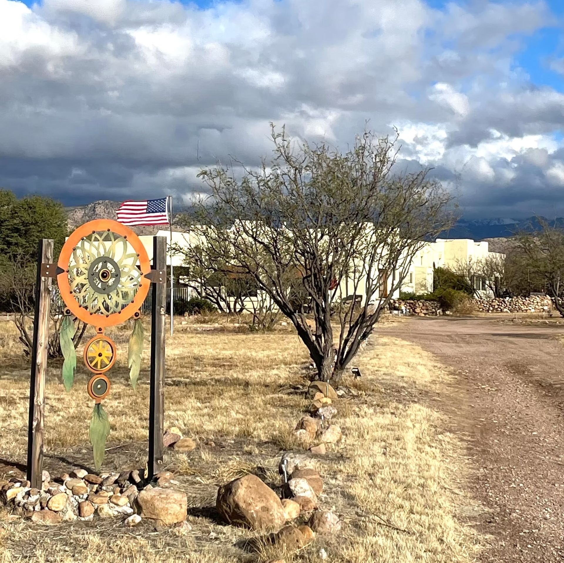 Desert roadside sign beside an American flag, tree, and clouds under a stormy sky