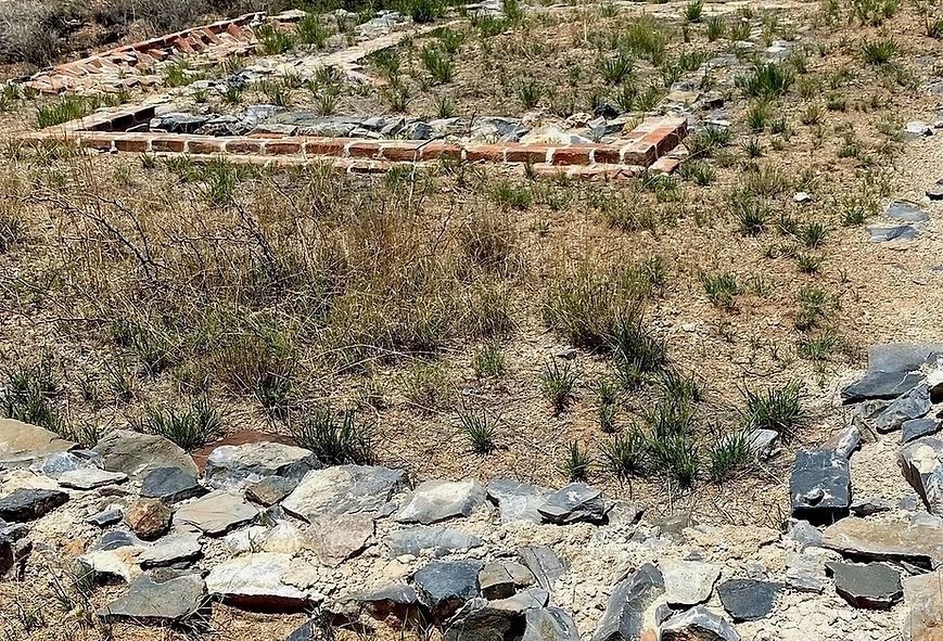 Rocky, dry hillside with sparse grass and a low brick border