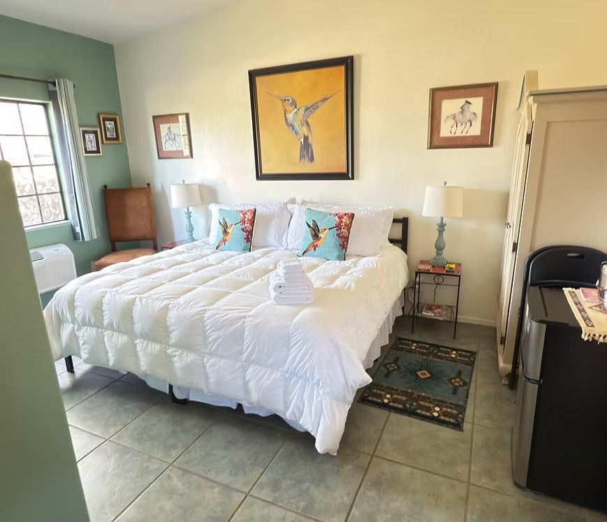 Cozy bedroom with white bed, colorful pillows, tiled floor, and framed bird art on the wall