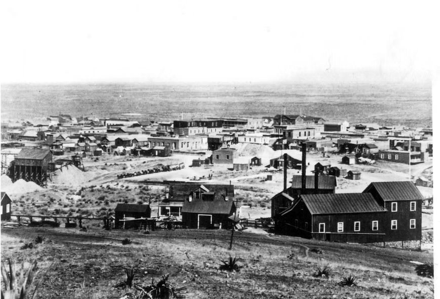 Black-and-white historic townscape with a church and clustered buildings stretching across a dry, open landscape