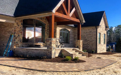 Stone house entrance with arched porch, steps, and paved driveway in daylight