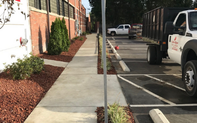 Sidewalk beside brick building with red mulch beds and parked trucks along the street