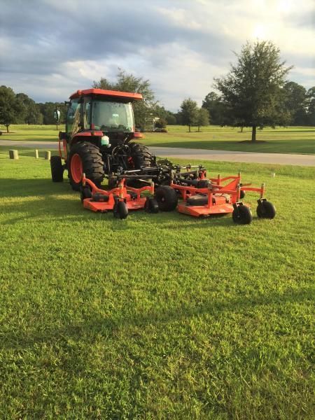 Red tractor with mower attachment on a grassy field under cloudy sky