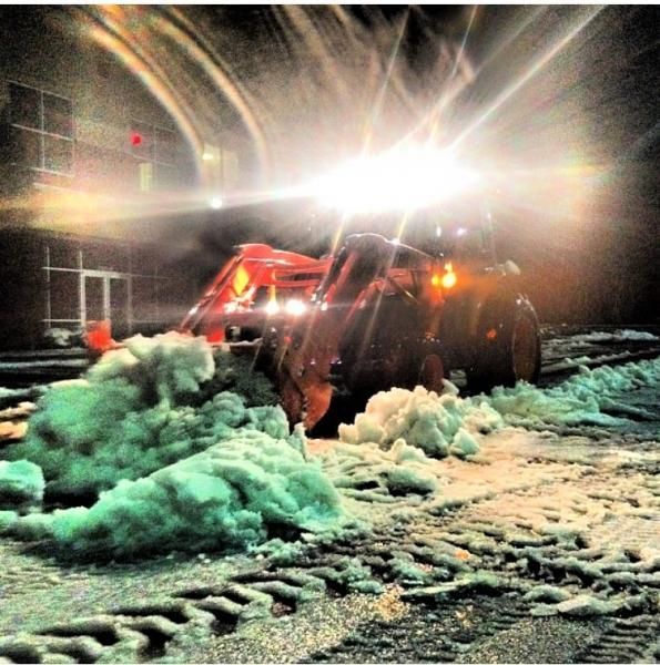 Snow plow clearing piled snow at night under bright headlights