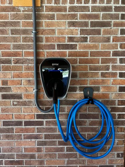 Wall-mounted electrical panel and outlet boxes beside a white exterior wall with conduit and cables.