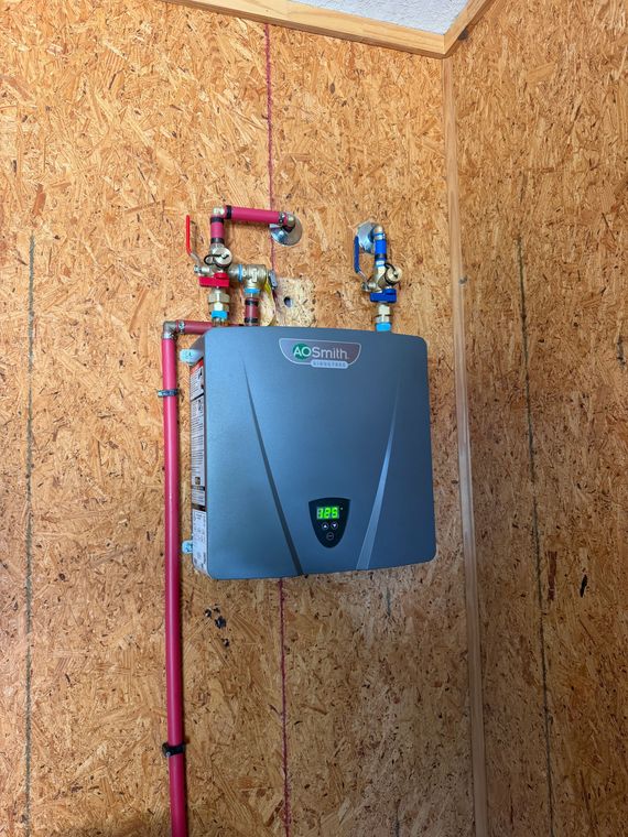 Water filtration setup with black tanks, blue piping, and a wall-mounted gauge in a utility room
