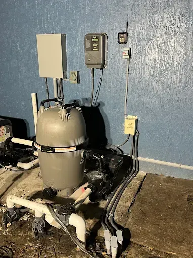 Basement water heater and pipes against a blue wall, with control boxes and wiring nearby