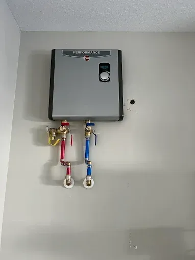 Wall-mounted water heater with red and blue pipes and valves on a gray wall.