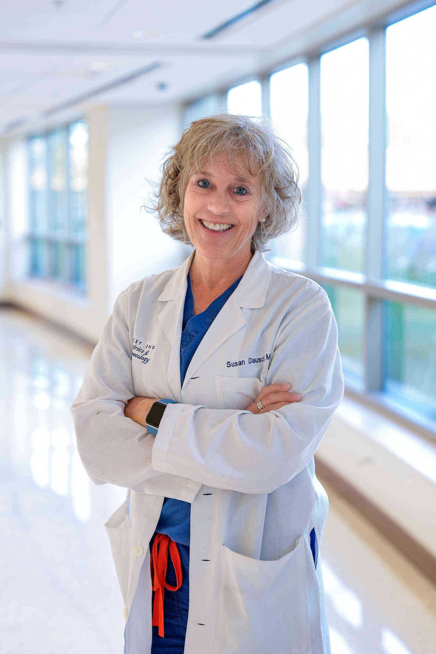A woman in a lab coat is standing in a hallway with her arms crossed.